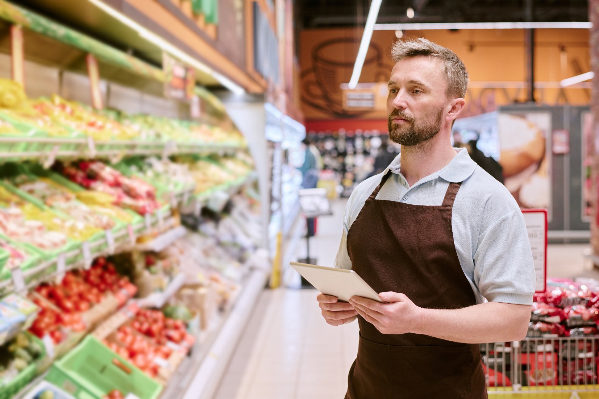 Employé de supermarché consultant une tablette devant le rayon fruits et légumes
