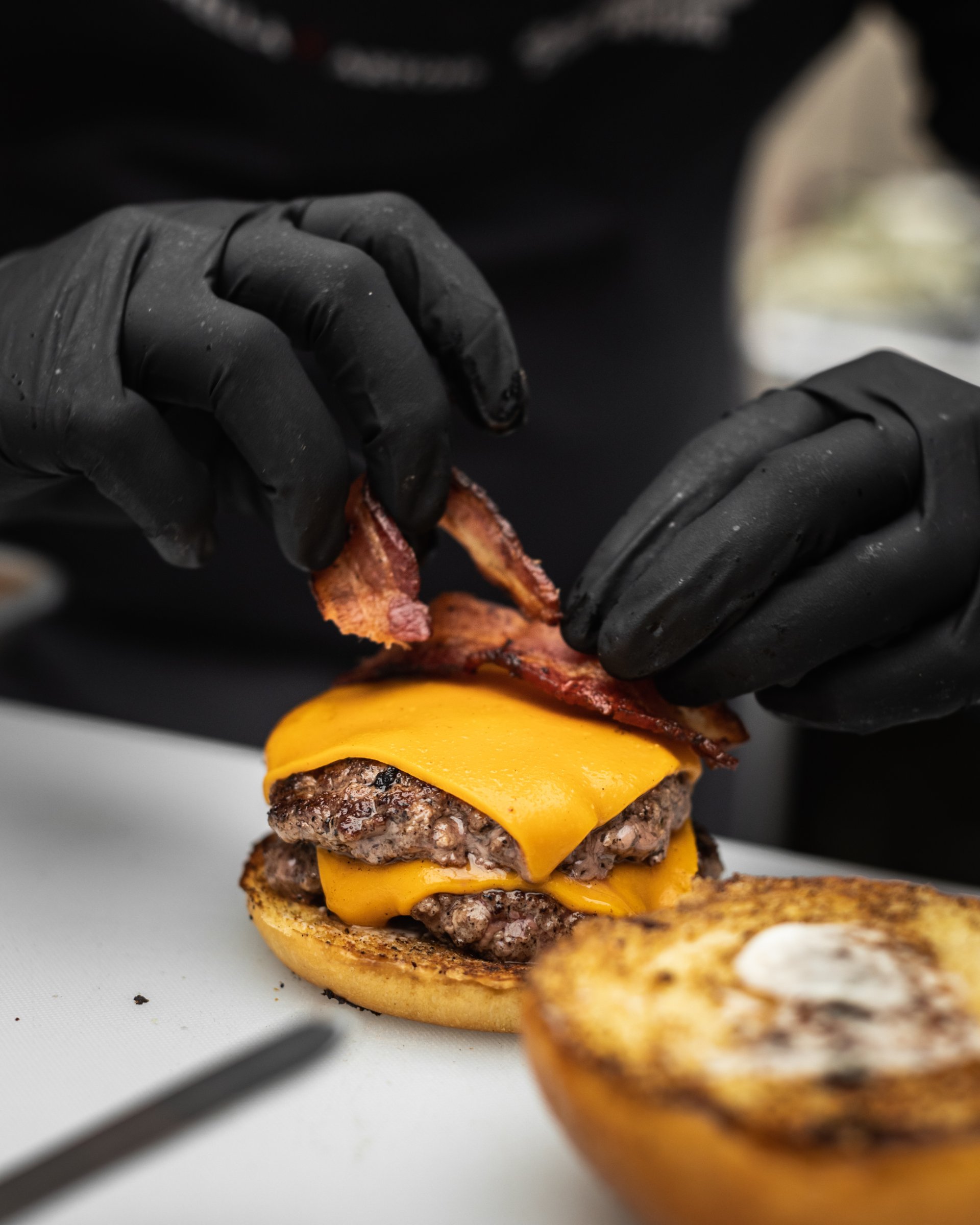 Cuisinier assemblant un burger au fromage et au bacon dans une cuisine de restauration rapide